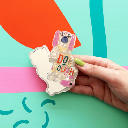 Hand holding a dog-shaped keychain with 'DOG ROUGH' text on a colorful background