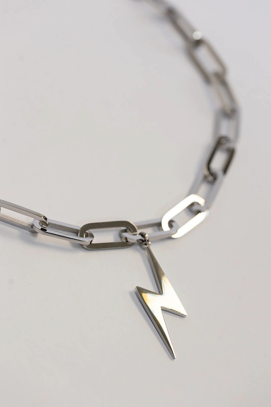 Silver chain bracelet with a lightning bolt charm on a light gray background