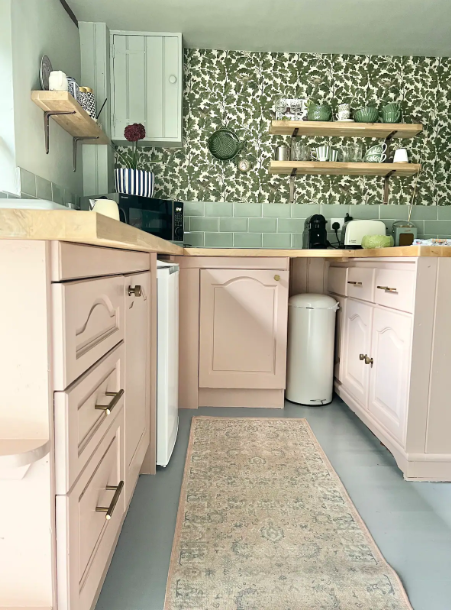 Kitchen with light pink cabinets, green patterned backsplash, and wooden shelves.