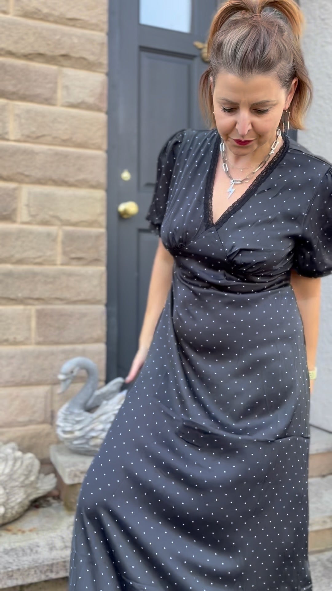 Woman wearing a black polka dot dress standing in front of a door.