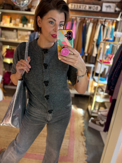 Woman taking a mirror selfie in a clothing store wearing a grey outfit with black sparkle bow button detailing