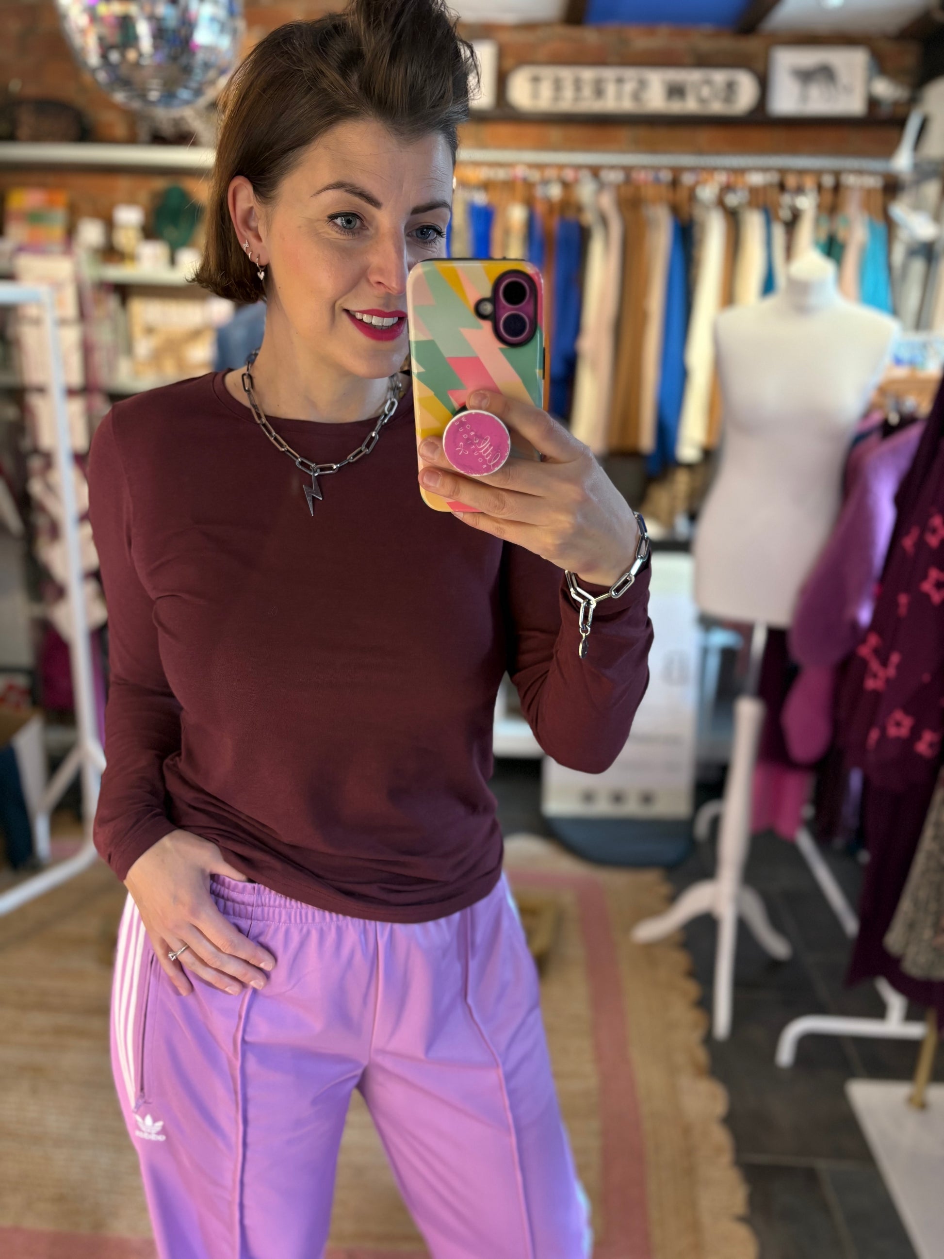 Woman taking a mirror selfie wearing a maroon long-sleeve top and pink pants in a clothing store.
