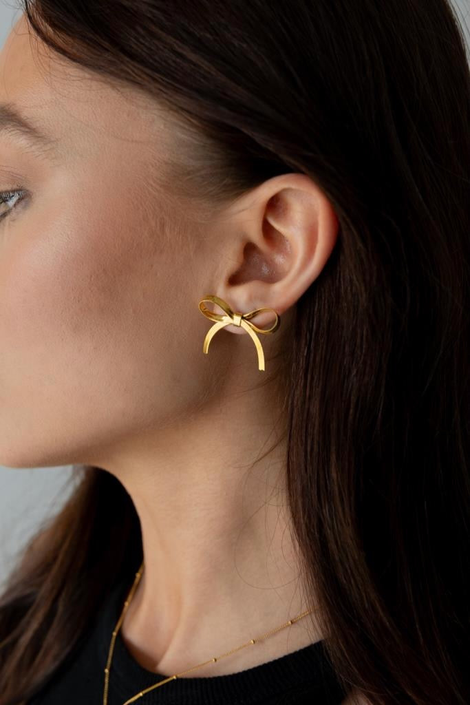 Close-up of a person wearing gold earrings with a neutral background