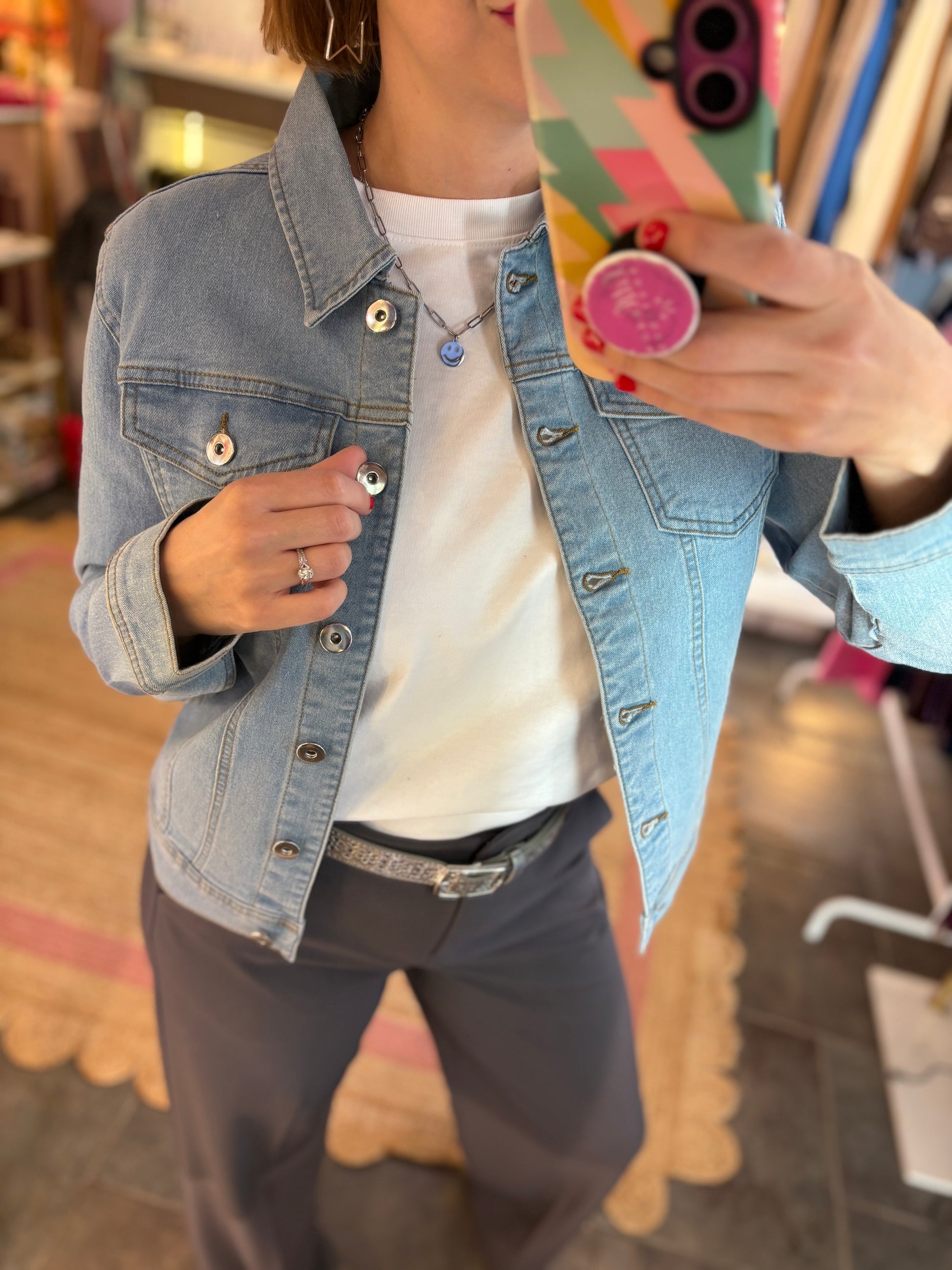 Person wearing a denim jacket and white shirt, taking a mirror selfie.