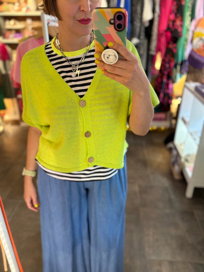 Person wearing a bright yellow cardigan over a striped shirt and blue pants, taking a mirror selfie.