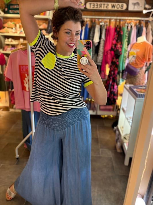 Person taking a mirror selfie wearing a striped shirt and blue pants in a store.