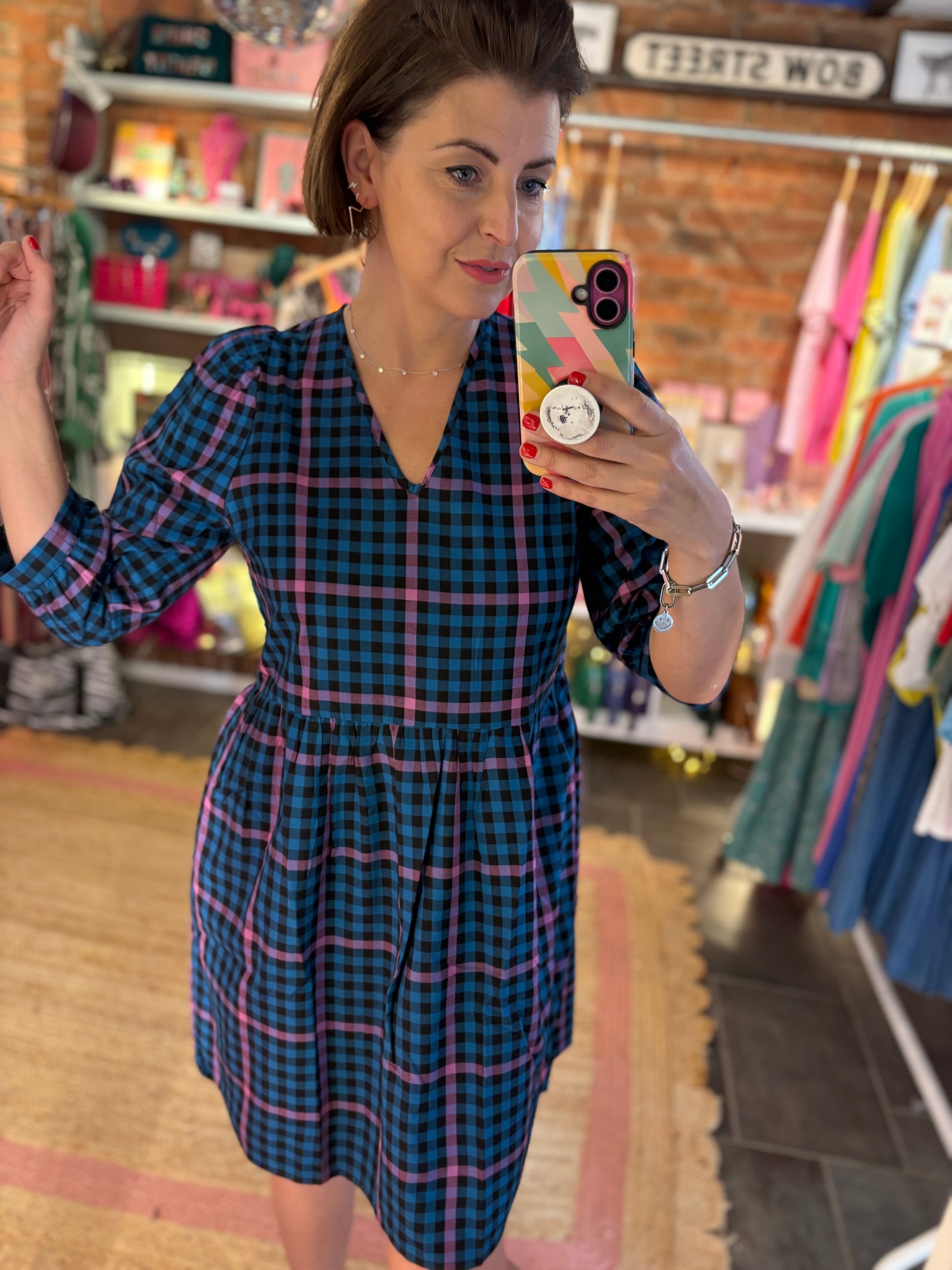 Woman taking a mirror selfie wearing a blue checkered dress in a store.