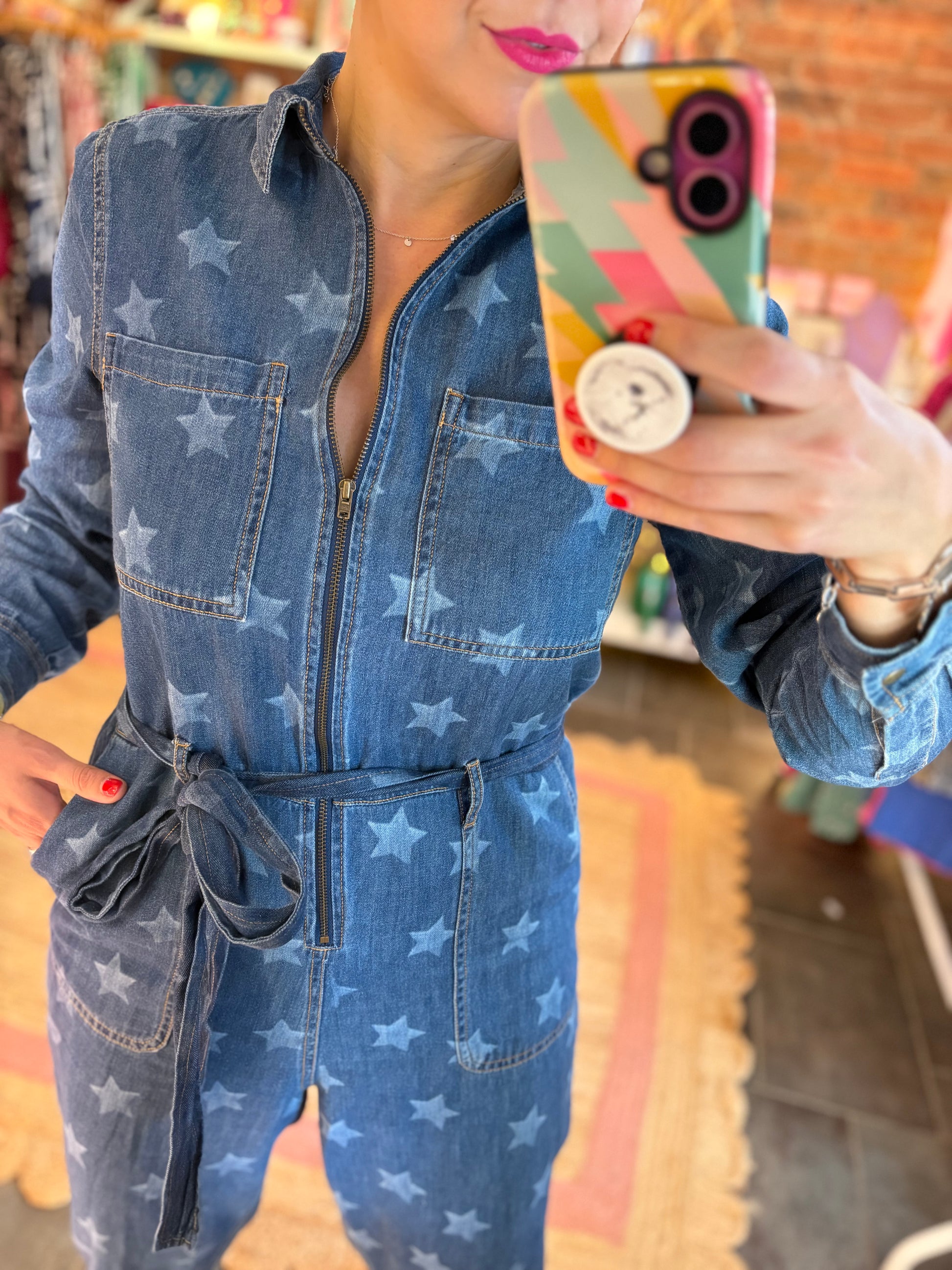 Person wearing a blue denim jumpsuit with star patterns, holding a colorful phone case.