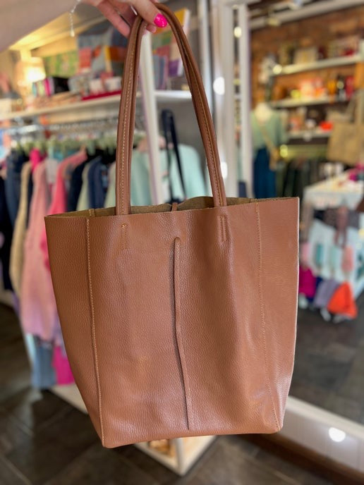 Brown tote bag held in front of a store interior with racks of clothes.
