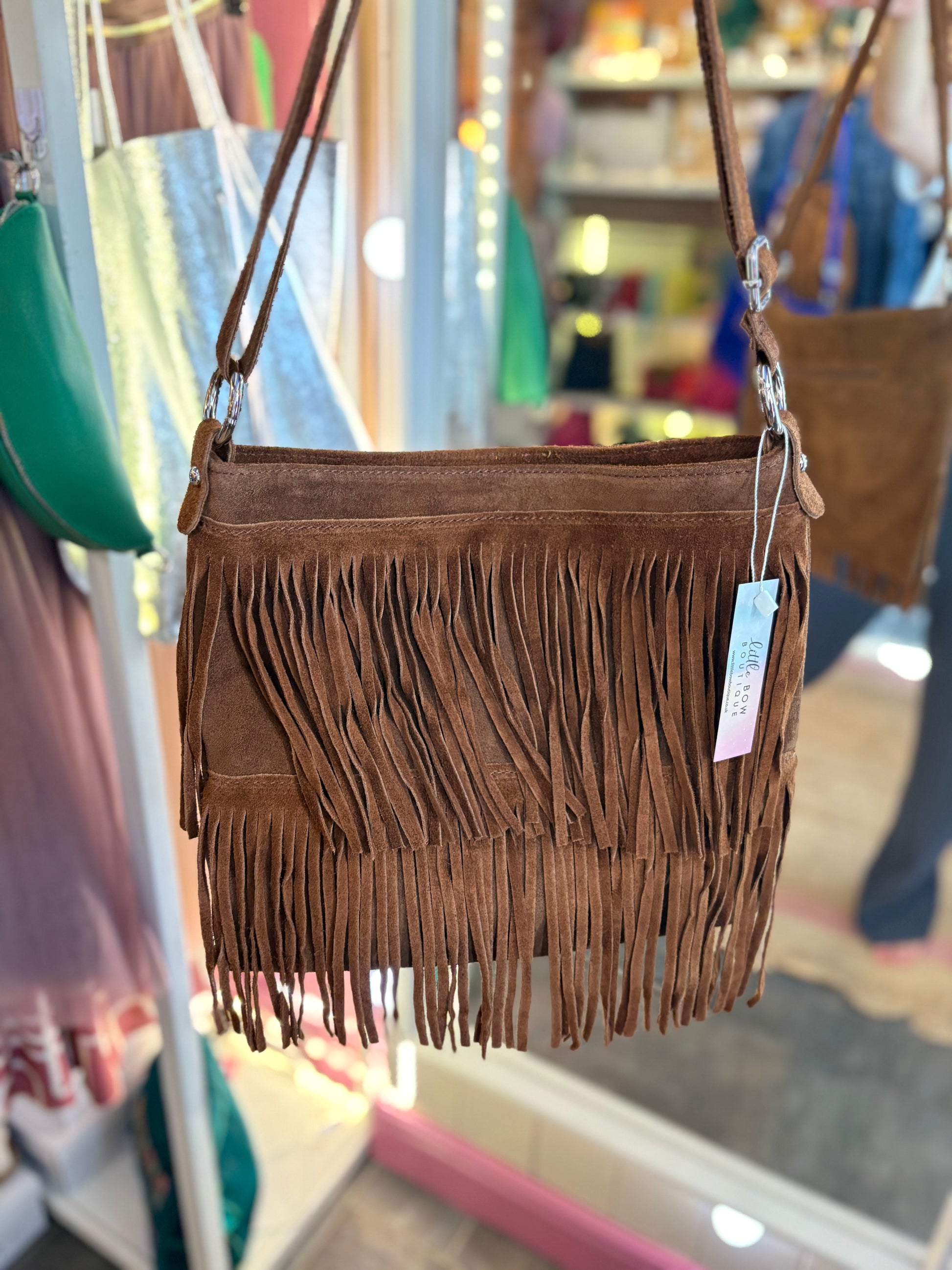 Tan Brown fringed suede handbag with a tag in a store setting