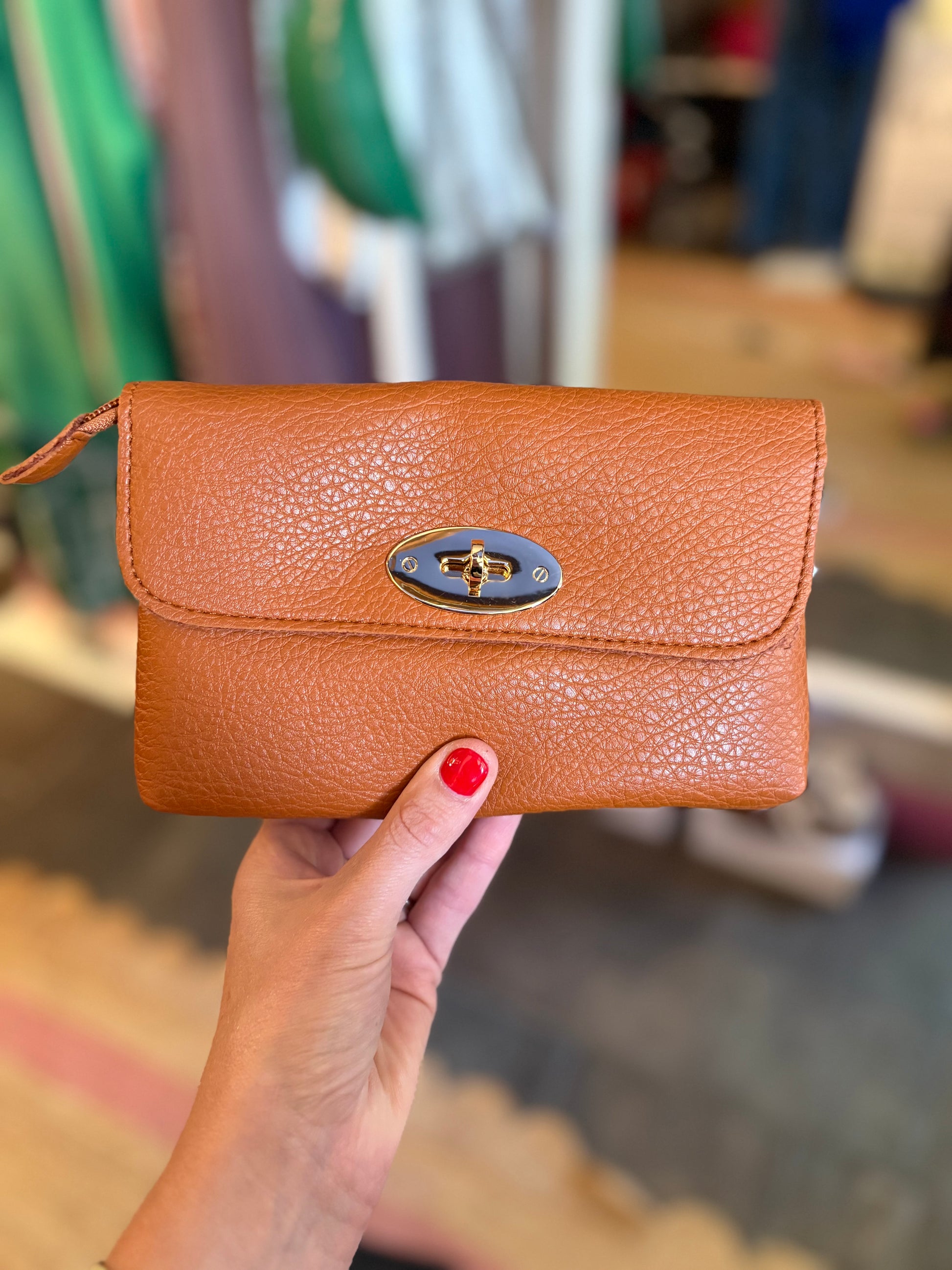 Brown leather clutch held by a hand with red nail polish, blurred indoor background