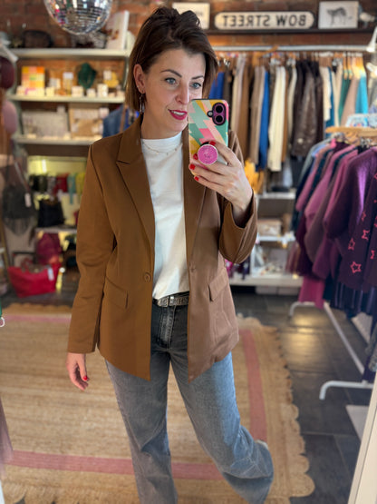 Woman taking a mirror selfie in a clothing store wearing a toffee brown blazer and jeans.