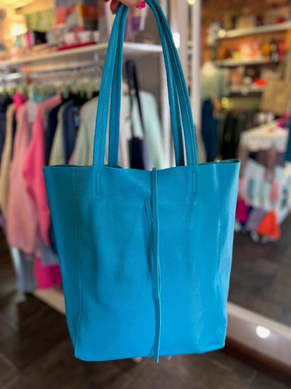Blue tote bag held in front of a clothing store with racks of clothes in the background.