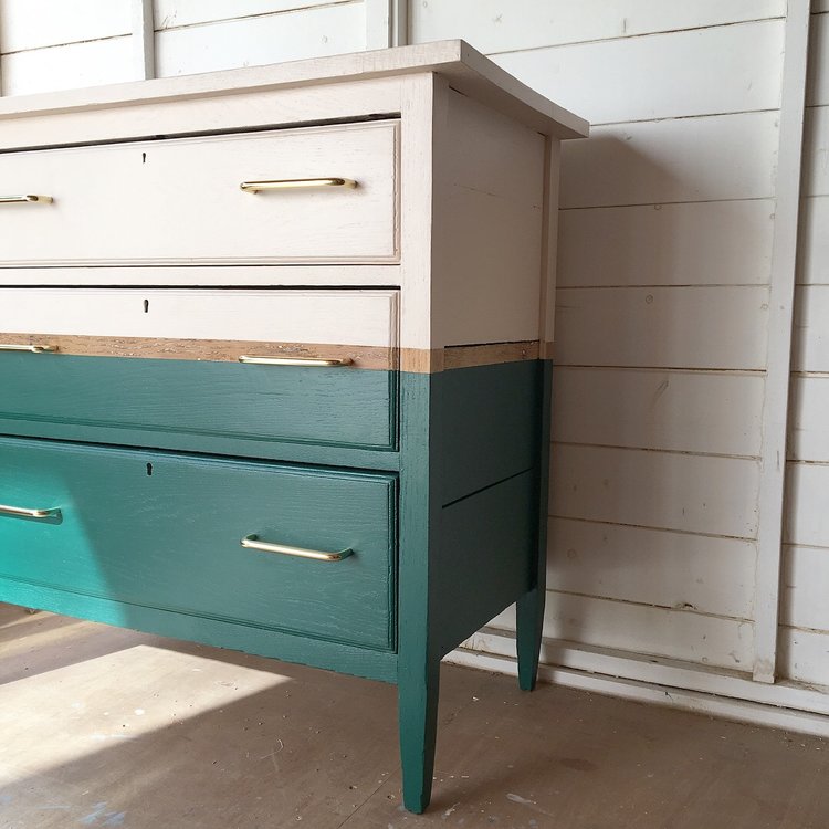 Two-toned dresser with white top and teal bottom against a wooden wall.