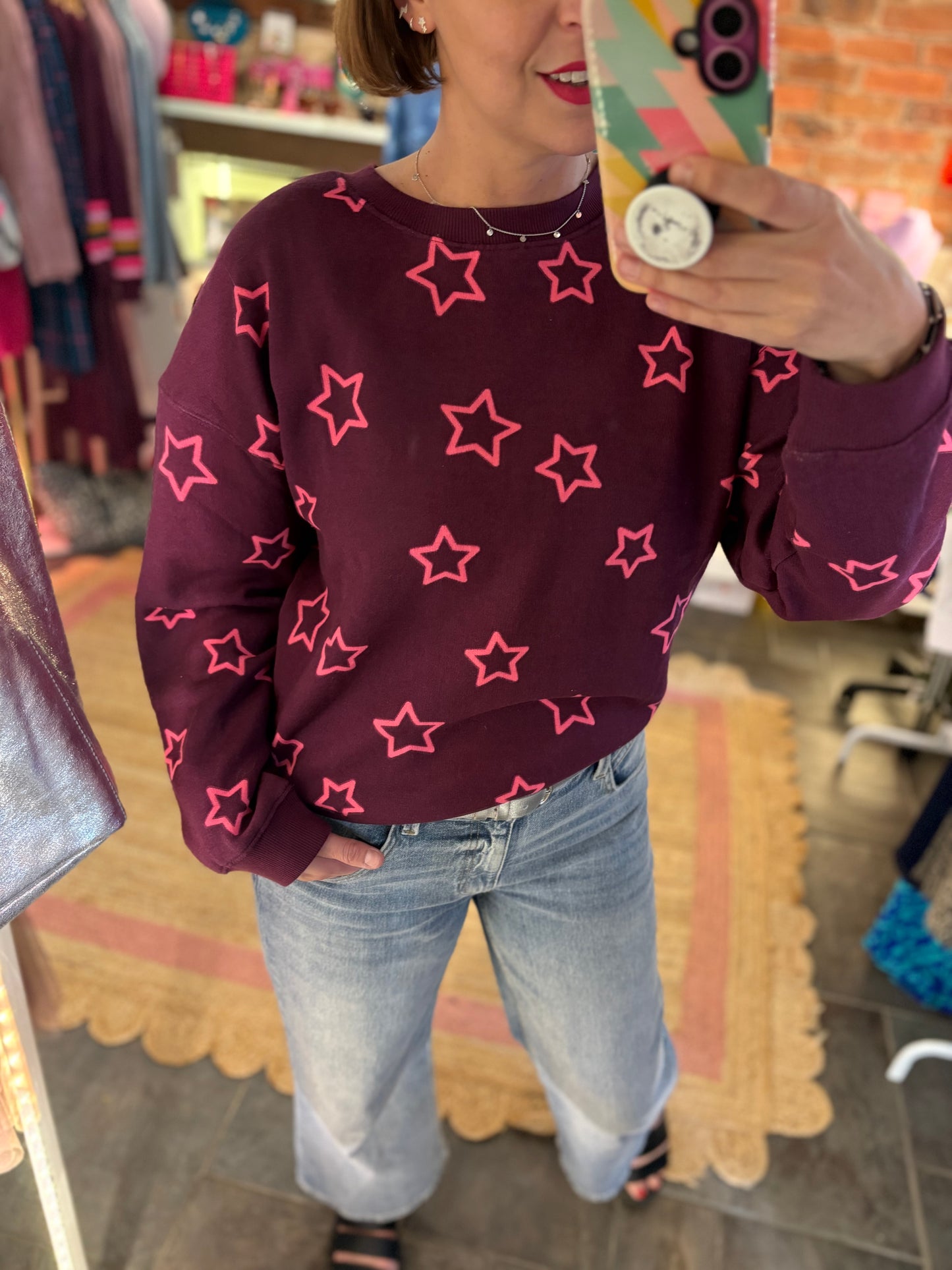 Person wearing a maroon sweatshirt with pink star patterns in a store setting.