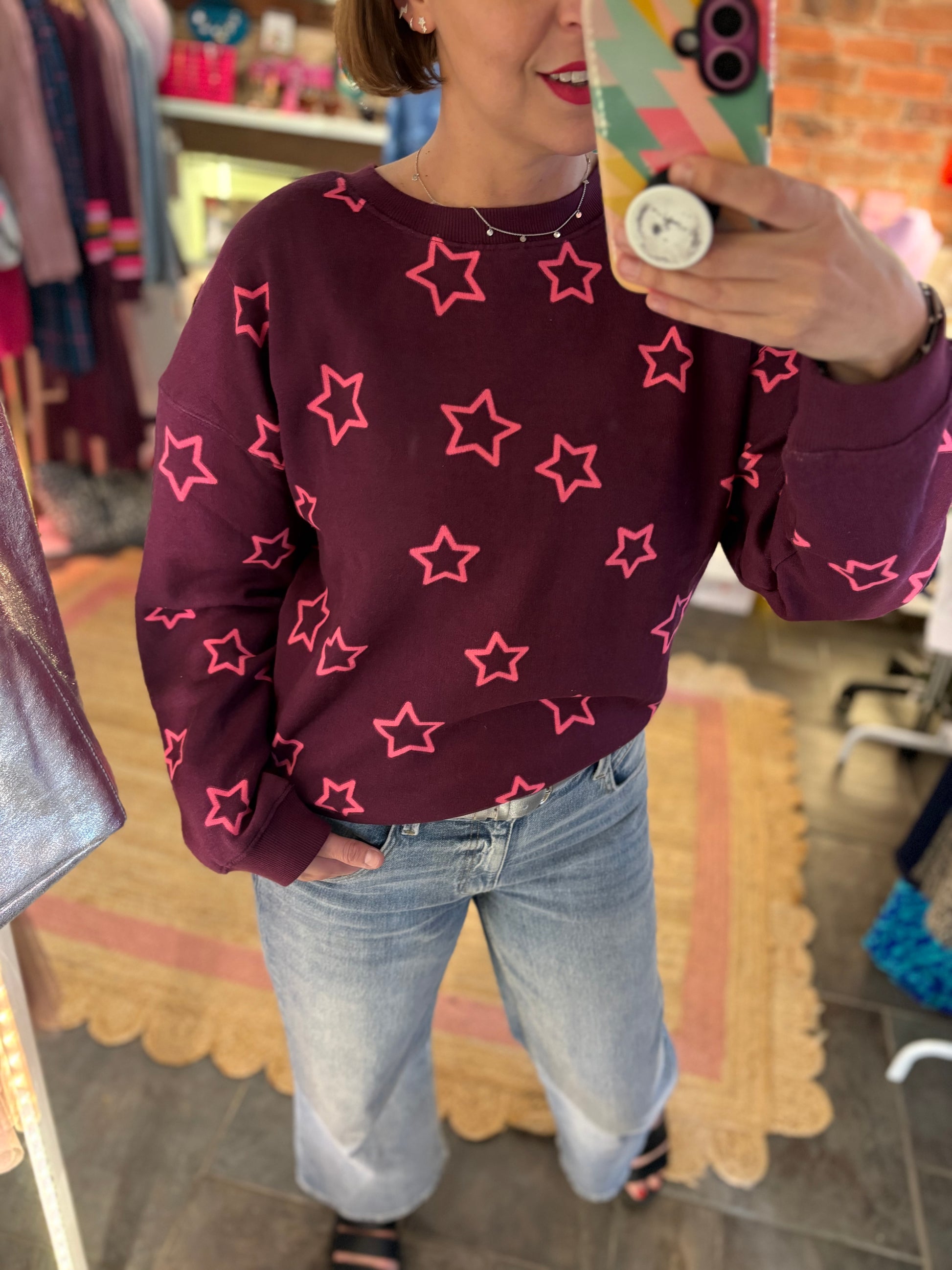 Person wearing a maroon sweatshirt with pink star patterns in a store setting.