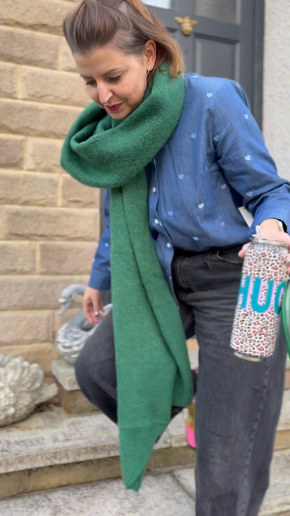 Woman wearing a green scarf and blue sweater, holding a bottle with a leopard print design.