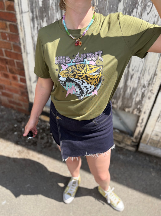 Person wearing an olive green graphic t-shirt with a leopard design outdoors.